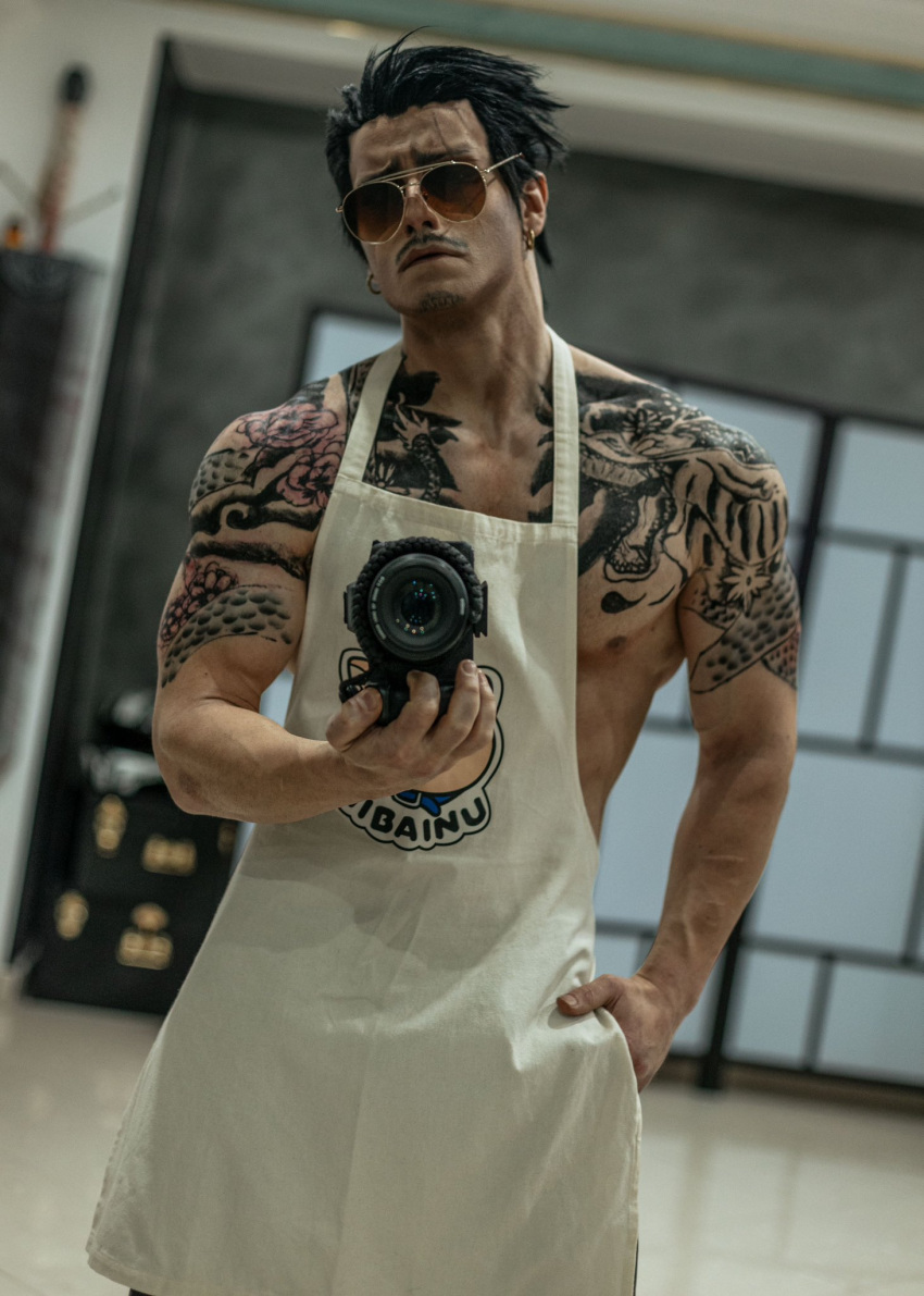 1boy apron arm_tattoo black_hair blurry blurry_background camera chest_tattoo closed_mouth cosplay cosplay_photo cowboy_shot dutch_angle earrings facial_hair gokushufudou hair_slicked_back highres holding holding_camera jewelry looking_at_viewer male_focus moustache muscular muscular_male nipple_slip nipples pectorals photo_(medium) short_hair sidepec solo sunglasses taryn_cosplay tatsu_(gokushufudou) tattoo white_apron